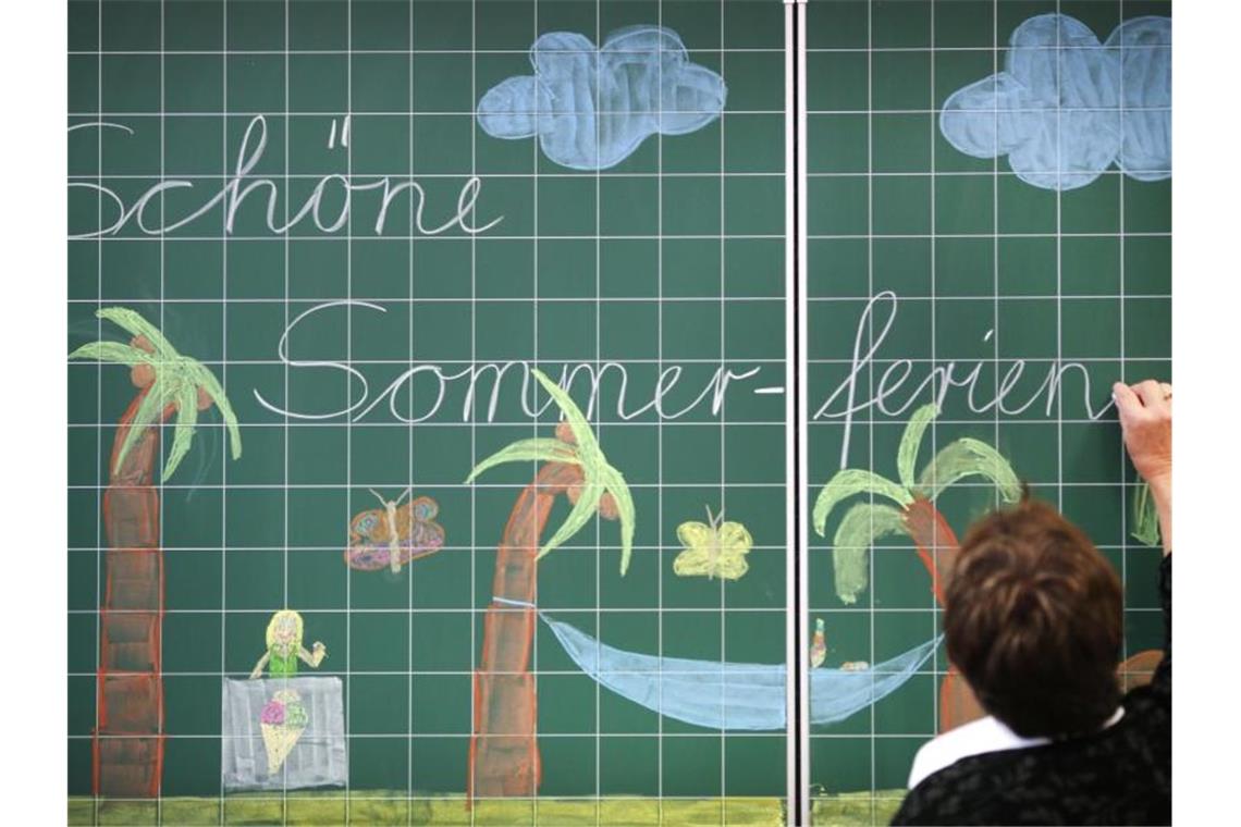 Eine Lehrerin schreibt „Schöne Sommerferien“ an eine Tafel in einer Grundschule. Foto: Ina Fassbender/dpa/Symbolbild