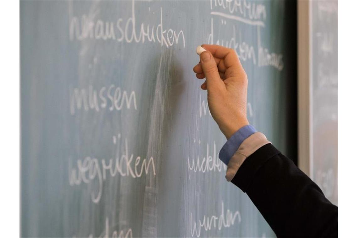 Eine Lehrerin steht in einem Klassenraum an einer Tafel und schreibt. Foto: Mohssen Assanimoghaddam/Archivbild