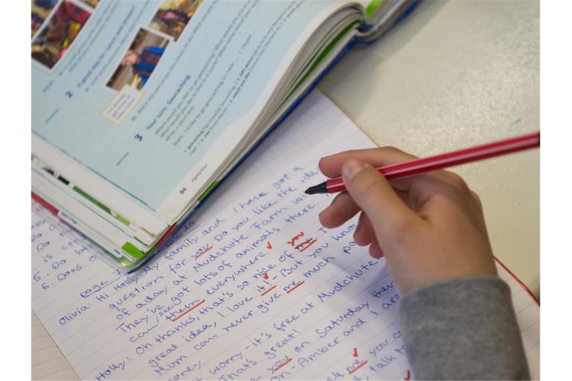 Eine lernende Person hält einen Rotstift in der Hand. Daneben liegen ein Heft und ein Buch. Foto: Marijan Murat/dpa/Archivbild