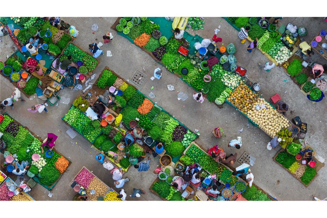 Eine Luftaufnahme zeigt das lebhafte Treiben auf einem Gemüsemarkt in Ahmedabad in Indien, wo Verkäufer frische Produkte anordnen und Kunden sich durch die engen Marktgassen bewegen.