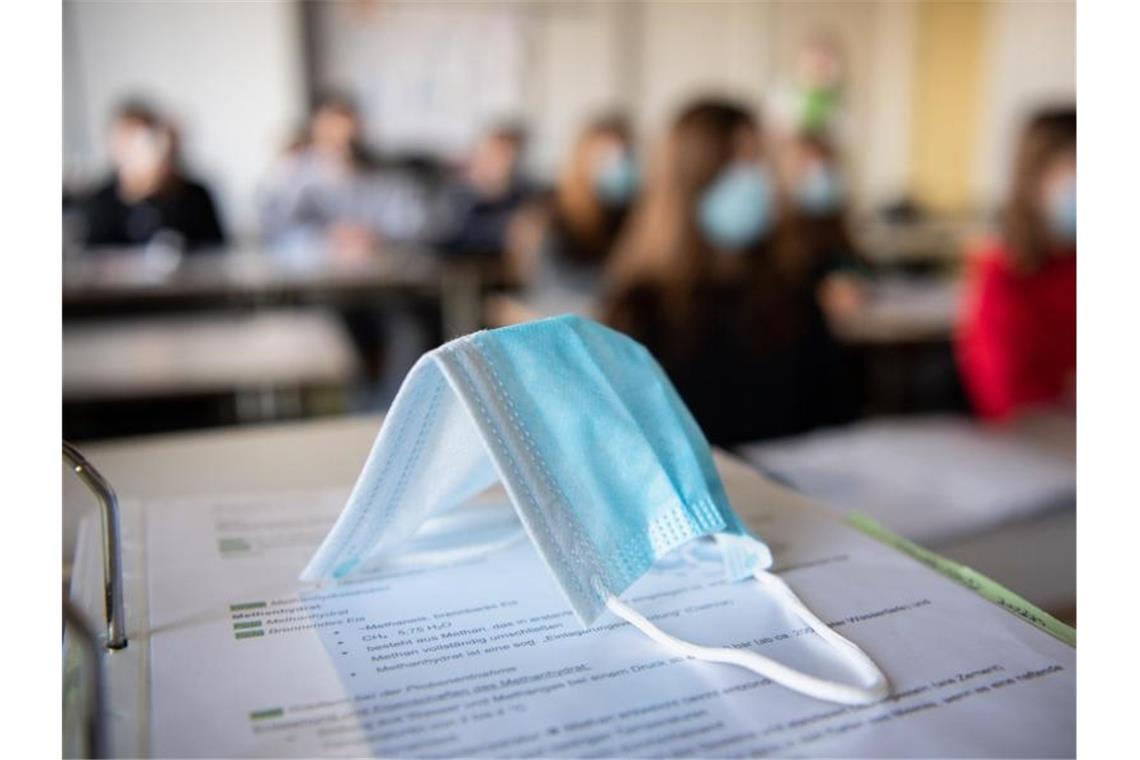 Eine Maske liegt im Unterricht an einem Gymnasium in München auf Schulunterlagen. Foto: Matthias Balk/dpa