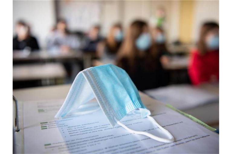 Eine Maske liegt im Unterricht auf Unterlagen. Foto: Matthias Balk/dpa/Illustration