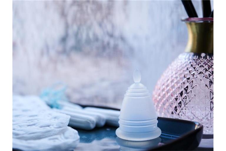 Eine Menstruationstasse, Slipeinlagen und Tampons verschiedener Hersteller liegen in einem Badezimmer. Foto: Annette Riedl/dpa