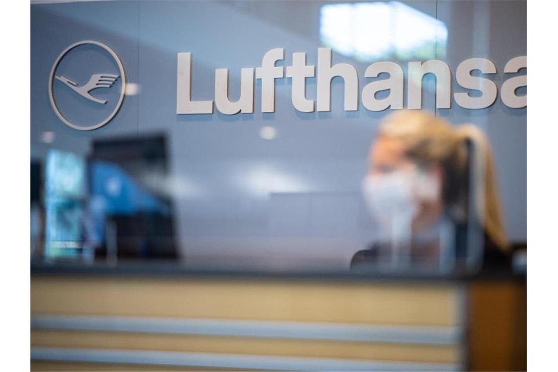 Eine Mitarbeiterin der Lufthansa sitzt mit ihrer Mund- und Nasenschutzmaske am Check-in. Foto: Guido Kirchner/dpa/Archivbild
