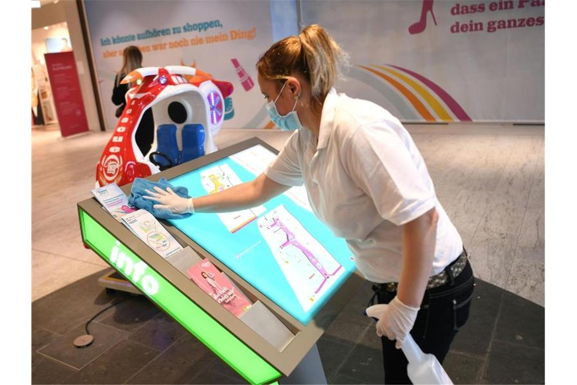 Eine Mitarbeiterin desinfiziert ein Informationsschild in einem Einkaufszentrum in Wien. Foto: Helmut Fohringer/APA/dpa