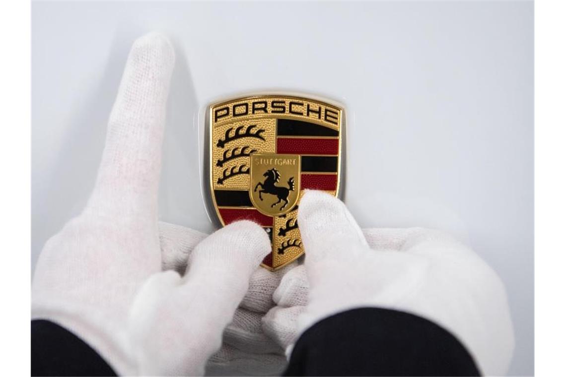 Porsche lässt Werke eine weitere Woche geschlossen Eine Mitarbeiterin hält ein Porsche-Emblem auf eine Motorhaube. Foto: Marijan Murat/dpa/Symbolbild