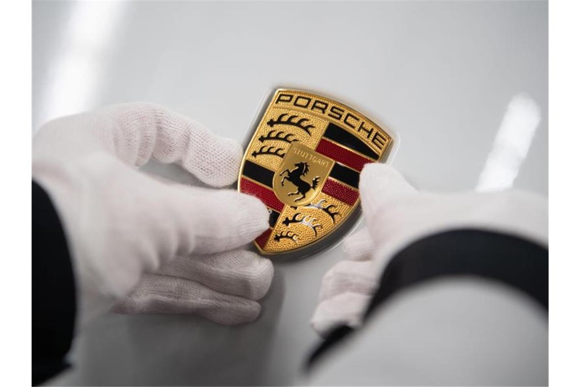 Eine Mitarbeiterin hält in der Produktion ein Porsche-Emblem auf die Motorhaube eines Porsche Taycan. Foto: Marijan Murat/dpa/Archivbild