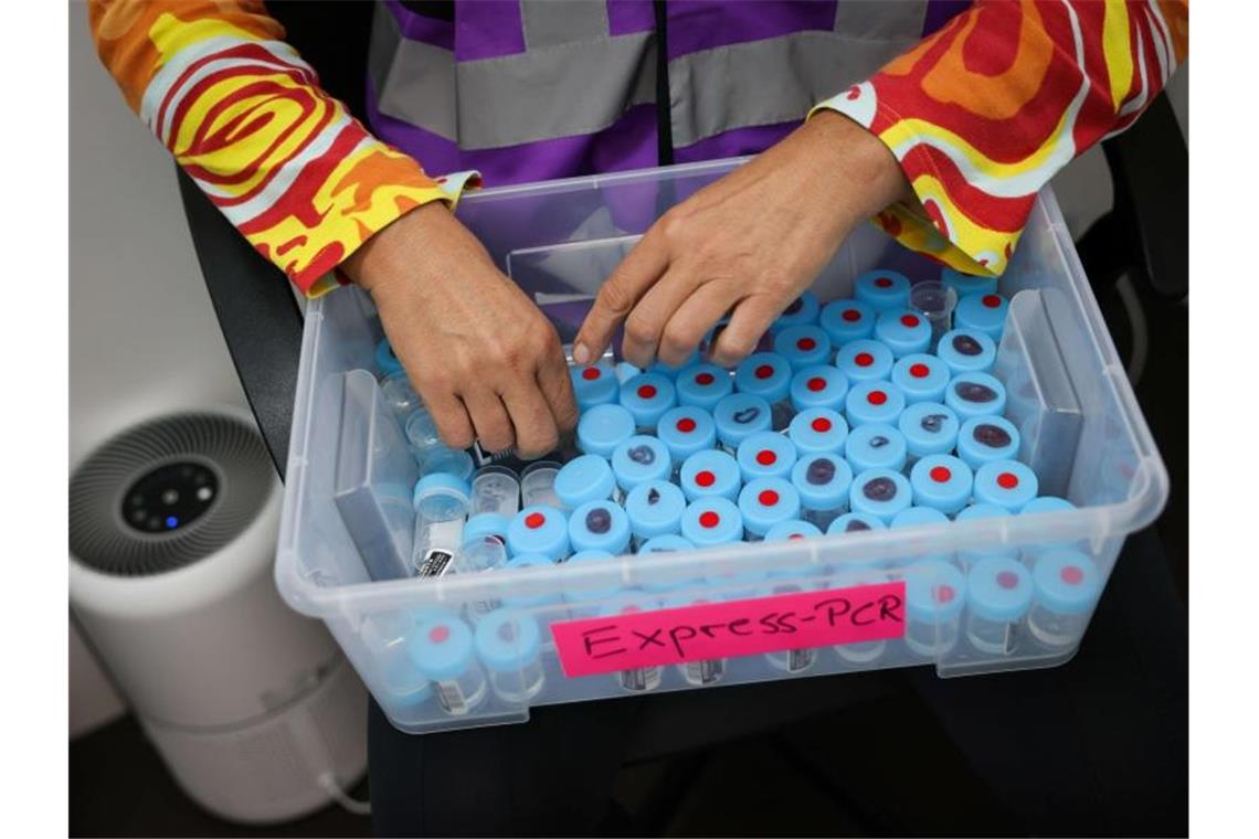 Eine Mitarbeiterin sortiert noch unbenutzte Behälter für einen PCR-Gurgeltest in einem Testcenter für Corona-Schnelltests (Antigentest) und Corona-PCR-Tests. Foto: Christian Charisius/dpa