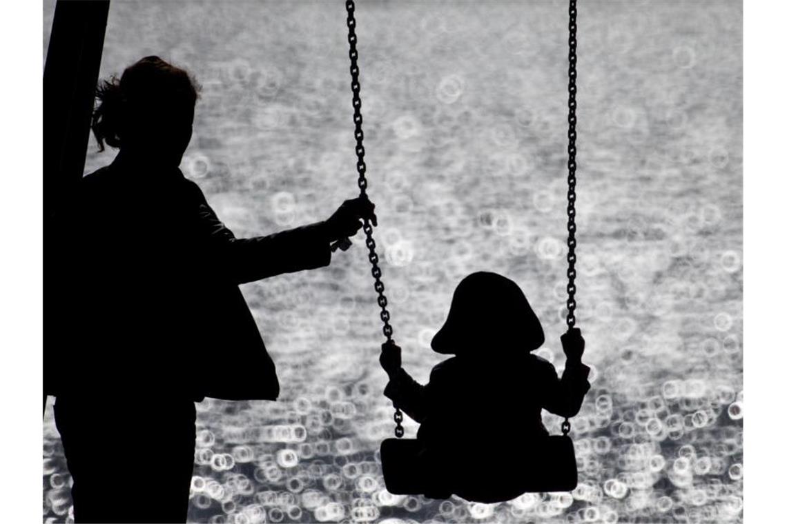 Eine Mutter schaukelt ihr Kind auf einem Spielplatz. Foto: Christian Charisius/dpa/Archivbild