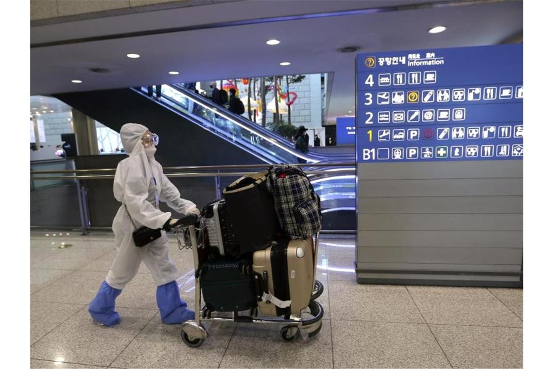 Eine Passagierin in Schutzkleidung schiebt am Flughafen Incheon einen Kofferwagen. Foto: Ahn Young-Joon/AP/dpa