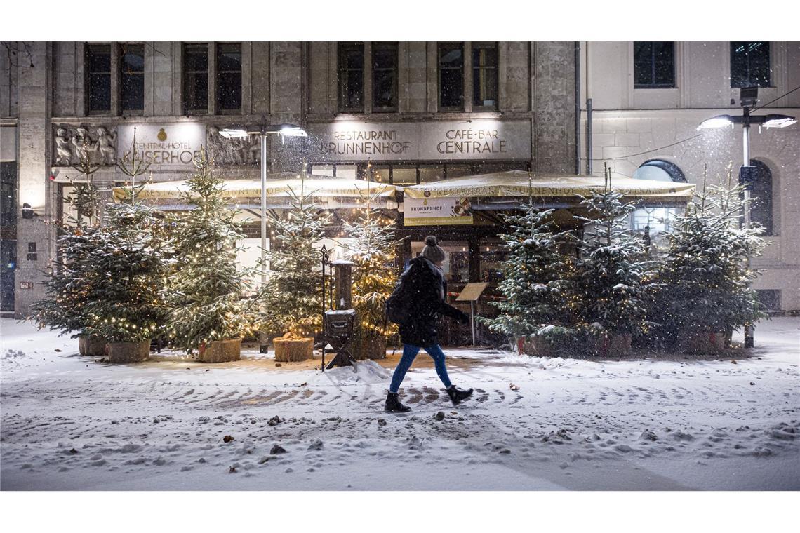 Eine Passantin geht am frühen Morgen im dichten Schneefall an Weihnachtsbäumen im Zentrum entlang.