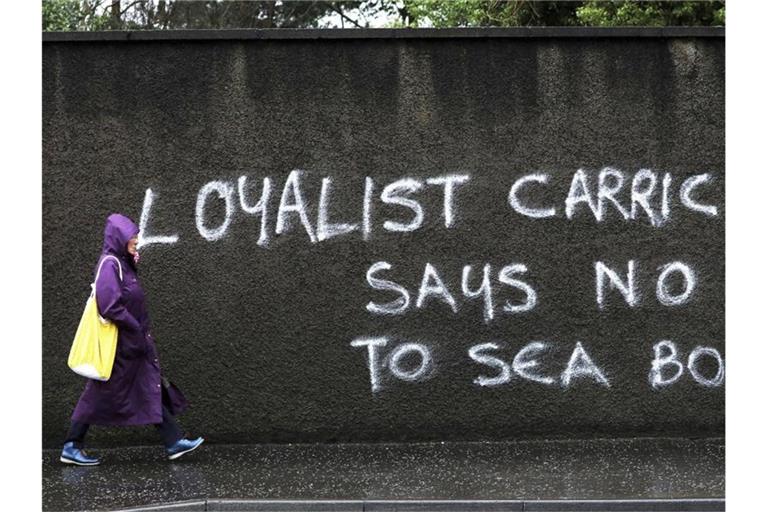 Eine Passantin geht in Belfast an einem Graffiti mit dem Schriftzug „Loyalist Carrick says no to Sea Border“ (Loyalist Carrick sagt Nein zur Seegrenze) vorbei. Foto: Peter Morrison/AP/dpa