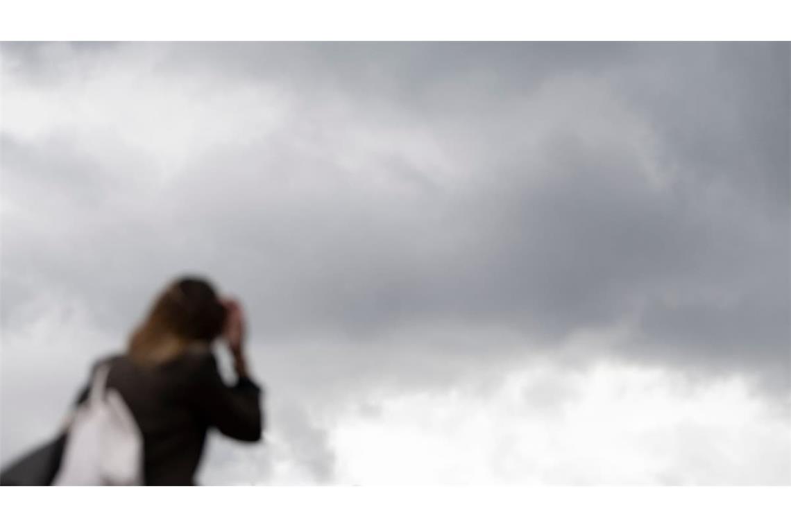 Eine Passantin geht in der Innenstadt vor grauen Wolken. (zu dpa: «Wo Wolken und Gewitter das Herbstwochenende trüben können»)