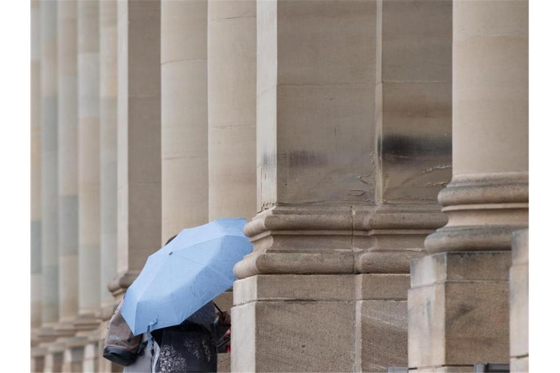 Eine Passantin hält auf dem Schlossplatz in einen Regenschirm in der Hand. Foto: Tom Weller/dpa/Archiv
