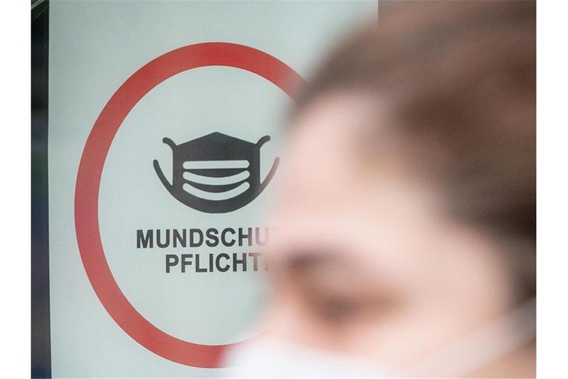 Eine Passantin mit Mund-Nasen-Schutz geht an einem Hinweisplakat mit der Aufschrift "Mundschutz Pflicht!" vorbei. Foto: Kay Nietfeld/dpa