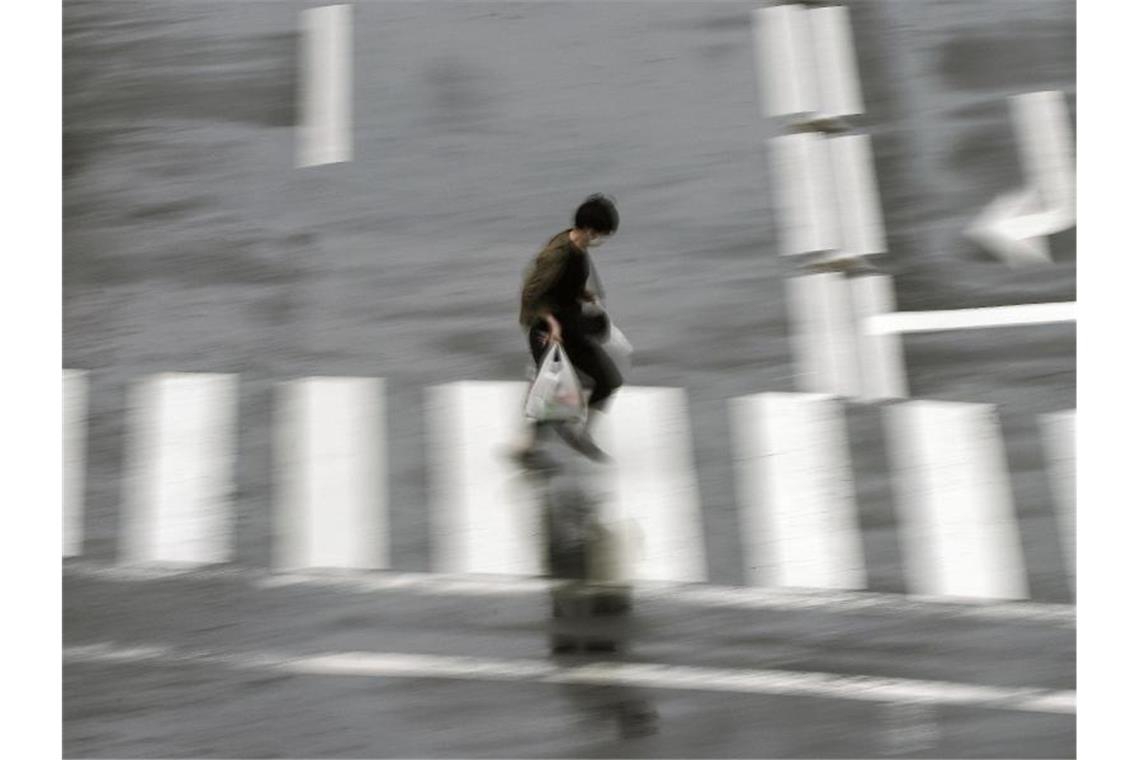 Olympia-Stadt Tokio erneut im Corona-Notstand Eine Person geht bei starkem Regen über einen Fußgängerüberweg im japanischen Tokio. Foto: Eugene Hoshiko/AP/dpa