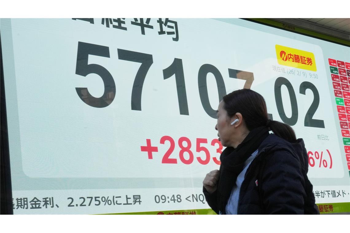 Eine Person geht vor einer elektronischen Börsentafel, die den japanischen Nikkei-Index anzeigt.