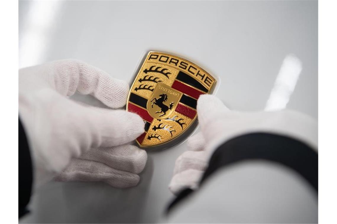 Eine Person hält ein Porsche-Emblem auf eine Motorhaube. Foto: Marijan Murat/dpa/Symbolbild