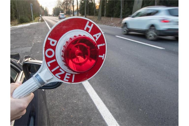 Eine Person hält eine Polizeikelle am Rand einer Fahrbahn. Foto: Armin Weigel/dpa/Archivbild