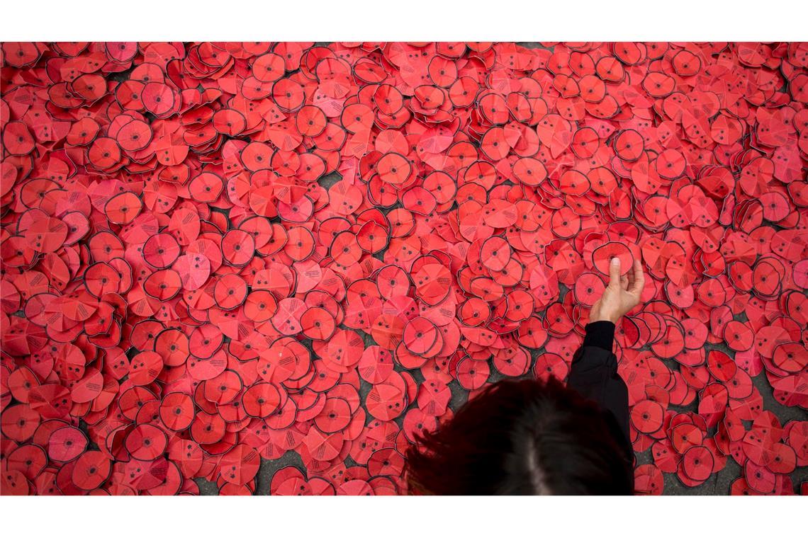 Eine Person hebt eine Papiermohnblume auf, die während einer Kundgebung gegen den Gaza-Krieg vor dem spanischen Außenministerium in Madrid auf dem Boden liegt.