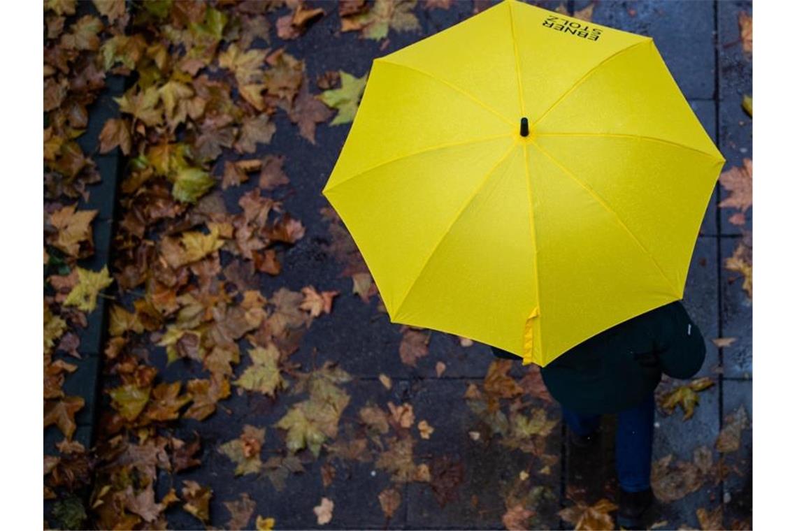 Eine Person läuft mit einem Regenschirm auf einem Gehweg. Foto: Tom Weller/dpa