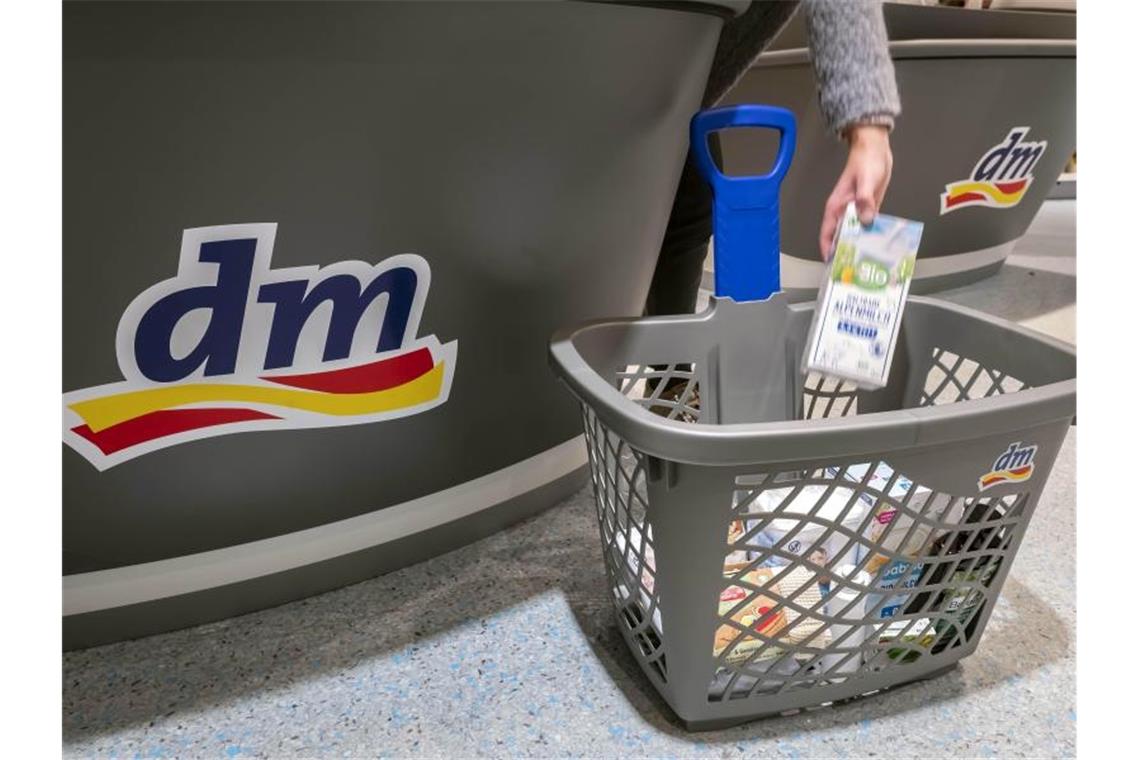 Eine Person legt in einer Filiale der Drogeriemarktkette dm im Kassenbereich ein Produkt in einen Einkaufskorb. Foto: Uli Deck/dpa