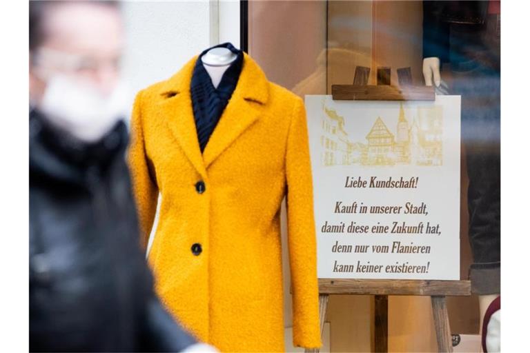 Eine Person mit Mund-Nasen-Schutz geht am Schaufenster eines Bekleidungsgeschäfts vorbei. Foto: Christoph Soeder/dpa/Archivbild