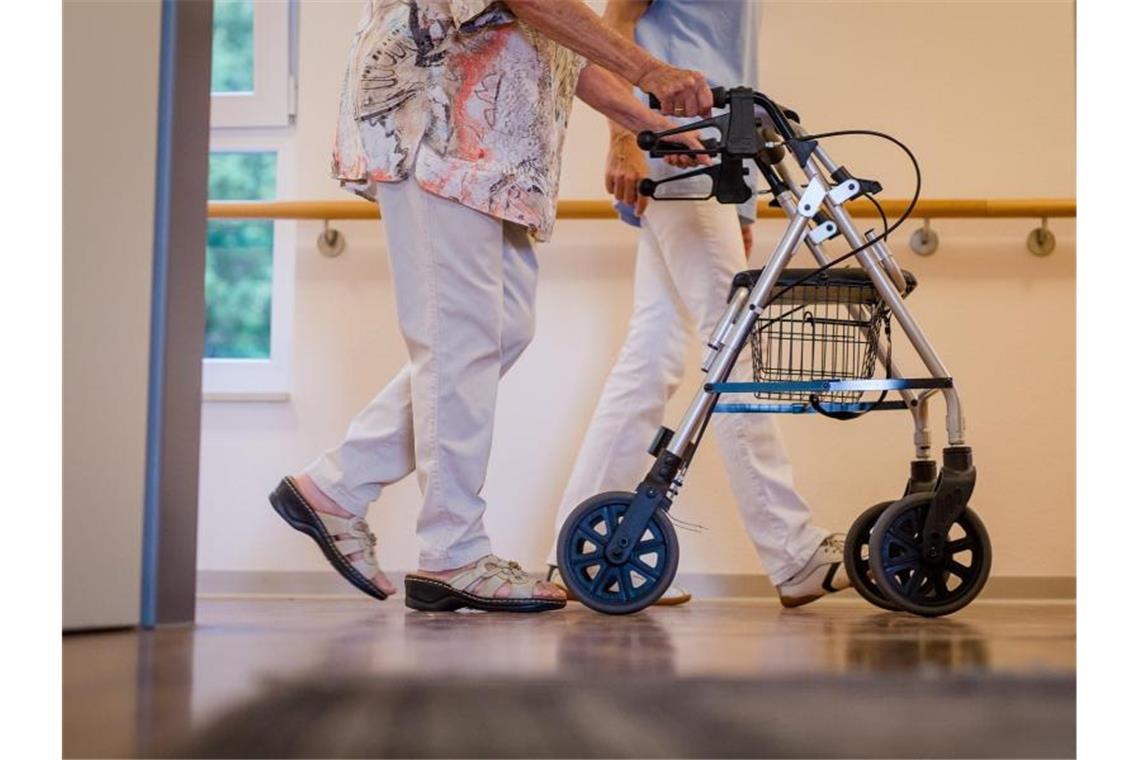 Eine Pflegekraft geht in einem Pflegeheim mit einer älteren Dame über einen Korridor. Foto: Christoph Schmidt/dpa