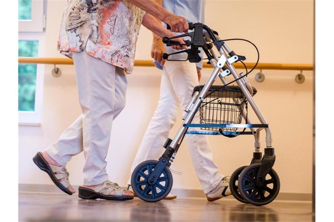 Pflegekräfte sollen mehr Geld bekommen Eine Pflegekraft geht in einem Pflegeheim mit einer älteren Dame über einen Korridor. Künftig sollen Beschäftige in der Alten- und Krankenpflege besser bezahlt werden. Foto: Christoph Schmidt