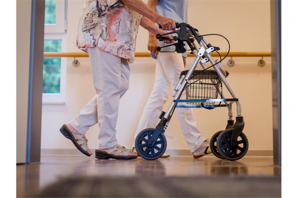 Besuchsverbote in Pflegeheimen werden gelockert Eine Pflegekraft geht in einem Pflegeheim mit einer älteren Dame über einen Korridor. Foto: Christoph Schmidt/dpa/Symbolbild