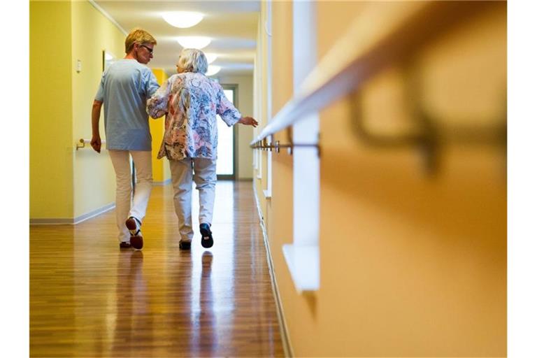 Eine Pflegerin geht in einem Pflegeheim mit einer älteren Dame über einen Korridor. Foto: Christoph Schmidt/Archivbild