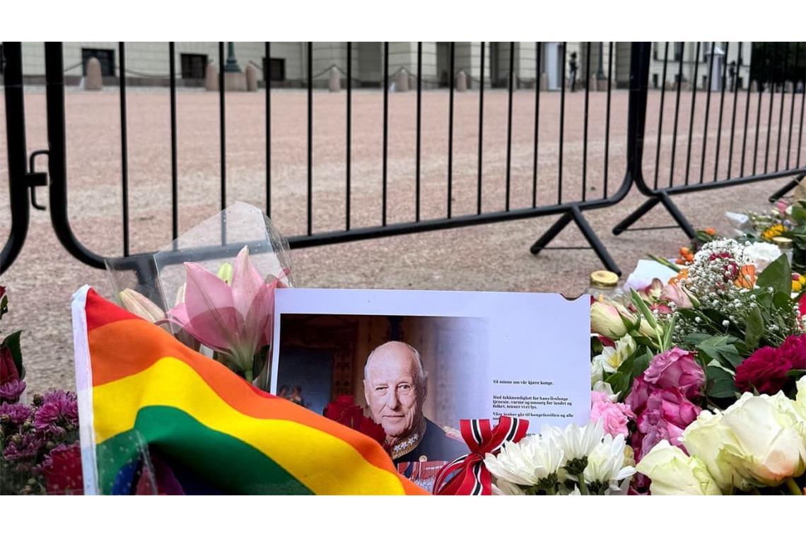 Eine Regenbogenfahne und ein Porträt des verstorbenen Königs Harald V. liegen vor dem Königlichen Schloss Oslo, wo zahlreiche Menschen zusammengekommen sind um zu trauern.
