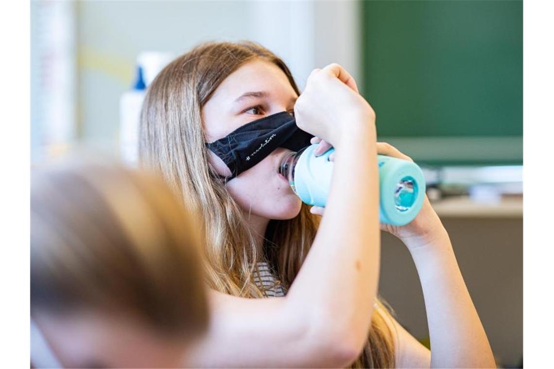 Eine Schülerin der Klasse 8a der Gesamtschule in Münster hebt ihre Mund- und Nasenmaske an, um etwas zu trinken. Foto: Guido Kirchner/dpa