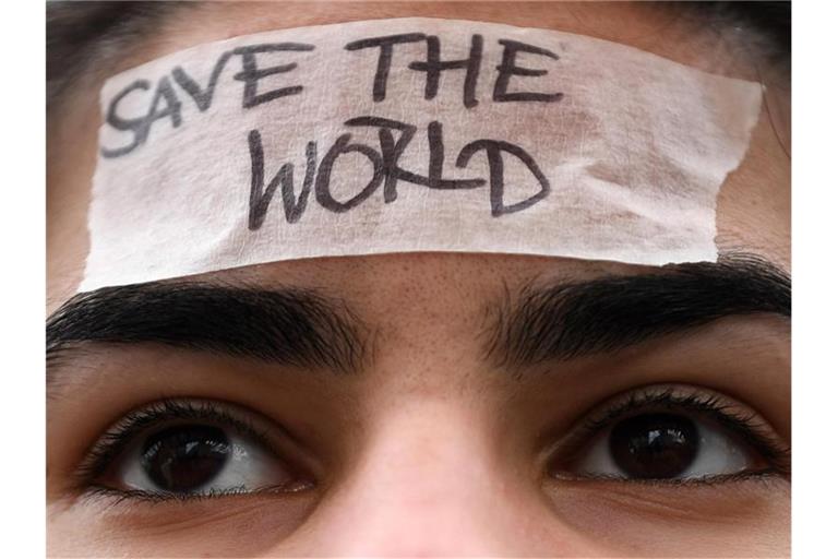 Eine Schülerin trägt ein Band mit der Aufschrift „Save the World“ auf ihrer Stirn. Foto: Hendrik Schmidt/zb/dpa/Archivbild