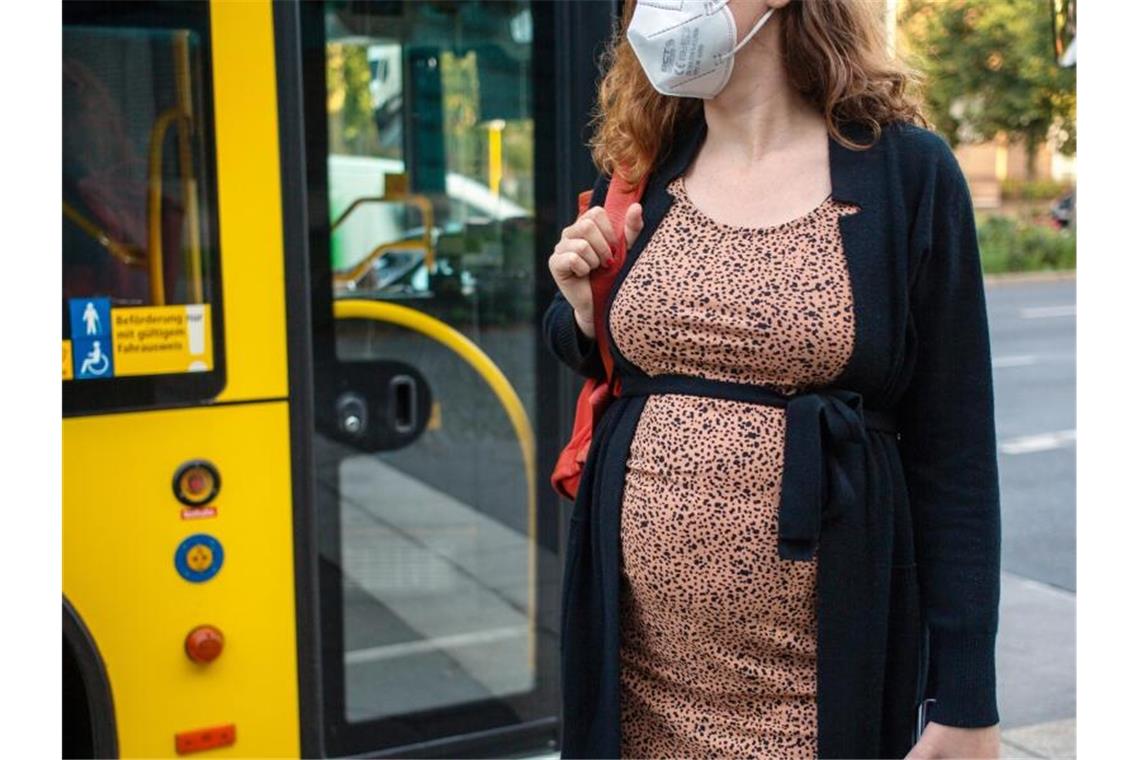 Eine schwangere Frau wartet mit Mund-Nasen-Schutz an einer Haltestelle auf dem Bus. Foto: Fernando Gutierrez-Juarez/dpa-Zentralbild/dpa