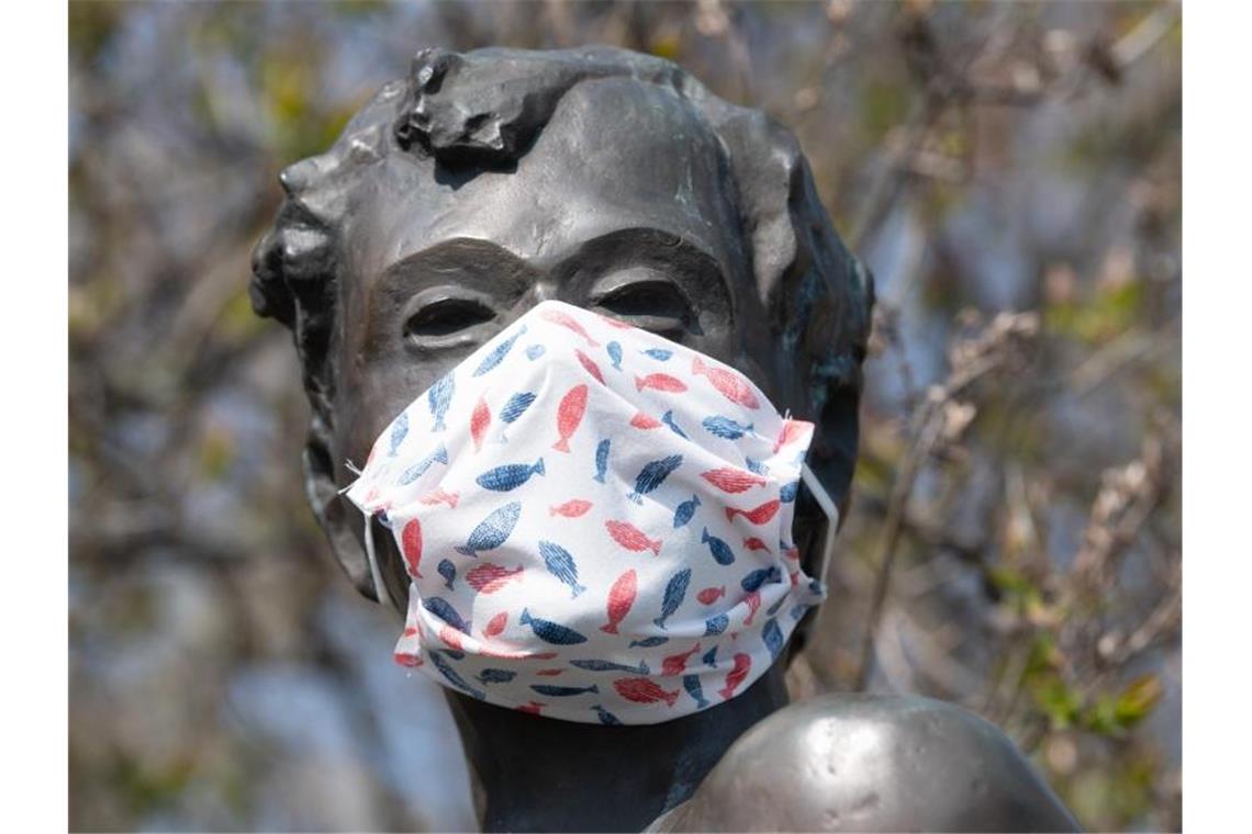 Eine selbstgebastelte Mundschutzmaske über der Kästner-Bronzeplastik in Dresden. Ingenieuren zufolge haben Staubsaugerbeutel für eine Maske der Marke Eigenbau hervorragende Filtereigenschaften. Foto: Sebastian Kahnert/dpa-Zentralbild/dpa