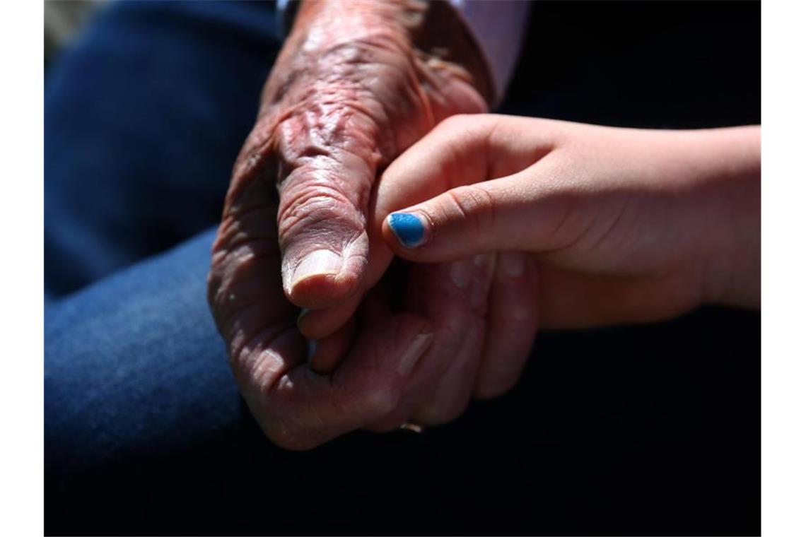 Eine Seniorin hält bei einem Verwandtenbesuch die Hand ihrer siebenjährigen Urenkelin. Foto: Karl-Josef Hildenbrand/dpa