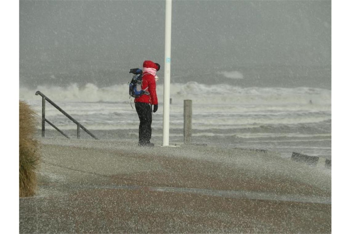 Eine Spaziergängerin auf Norderney blickt auf die Wellen der vom Sturm aufgepeitschten Nordsee. Foto: Volker Bartels/dpa