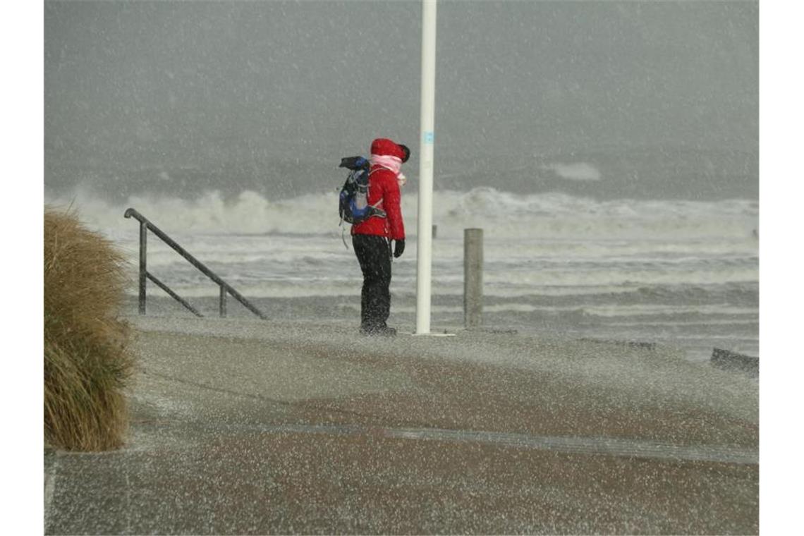 Tief „Marie“ wirbelt mit Wind und Schnee nach Deutschland Eine Spaziergängerin blickt auf Norderney auf den Nordstrand und die Wellen der vom Sturm aufgepeitschten Nordsee, während ein Hagelschauer über sie heruntergeht. Foto: Volker Bartels/dpa