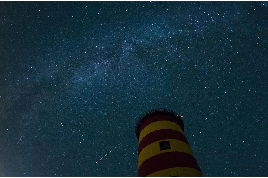 Woher kommt der Mensch? Eine Spurensuche im Kosmos Eine Sternschnuppe leuchtet im August 2015 über dem Pilsumer Leuchtturm in Niedersachsen am Nachthimmel.