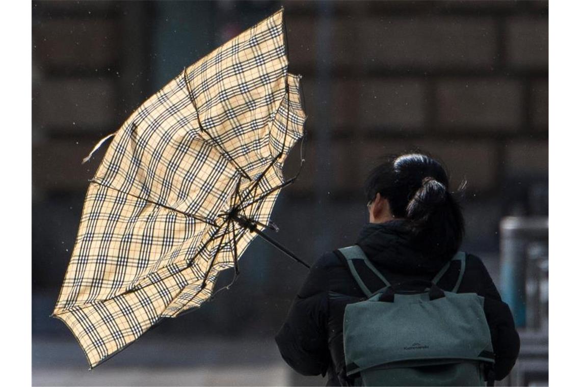 Eine Sturmböe erfasst den Schirm einer Frau. Foto: Boris Roessler/dpa/Symbolbild