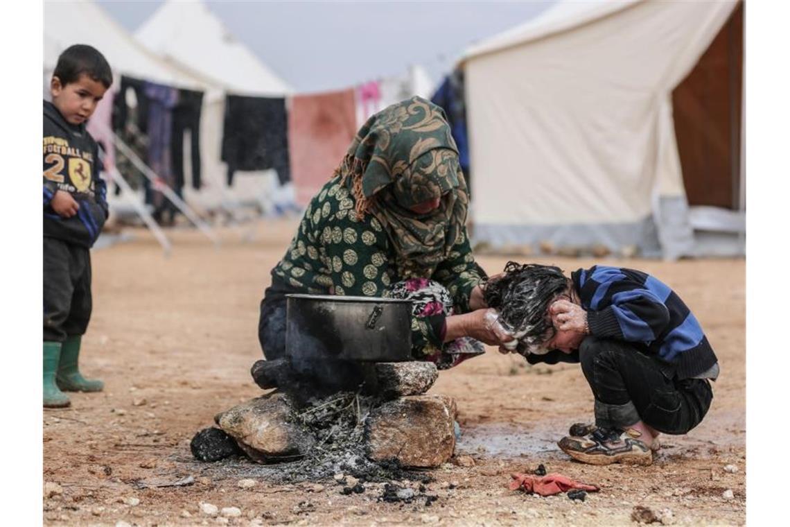 Eine Syrerin wäscht ihr Kind in einem Behelfslager für Familien, die durch Bombenangriffe vertrieben wurden. Foto: Anas Alkharboutli/dpa