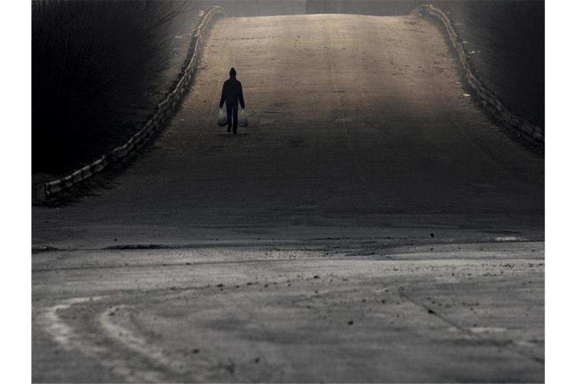 Krieg gegen die Ukraine: So ist die Lage Eine Szene außerhalb Kiews: Ein Mann trägt Einkaufstaschen, während dichter Rauch aus einem durch russisches Bombardement zerstörten Lagerhaus Schatten auf die Straße wirft. Foto: Vadim Ghirda/AP/dpa