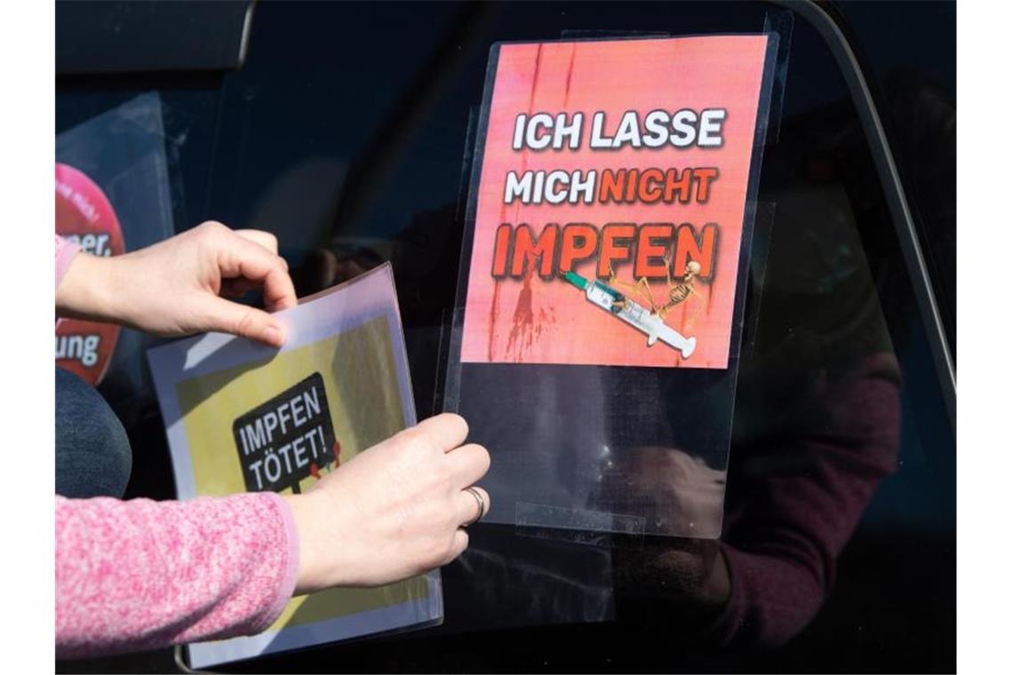 Eine Teilnehmerin eines Autokorsos stattet ihr Fahrzeug mit Anti-Impf-Schildern aus. Foto: Sebastian Kahnert/dpa-Zentralbild/dpa