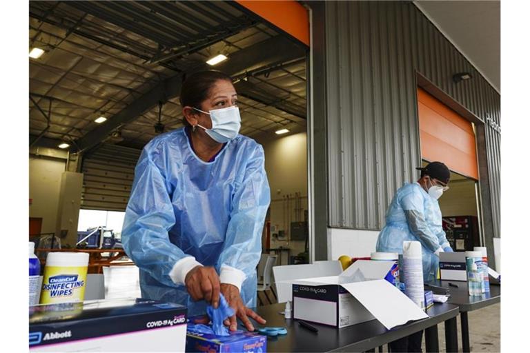Eine Testmitarbeiterin nimmt sich ein Paar Handschuhe, während sie sich auf die Durchführung von COVID-19-Antigentests in Texas vorbereitet. Foto: Denise Cathey/The Brownsville Herald/dpa
