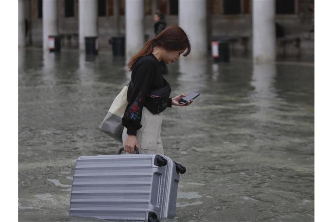 Eine Touristin trägt ihr Gepäck durch das Hochwasser auf dem Markusplatz. Foto: Luca Bruno/AP/dpa