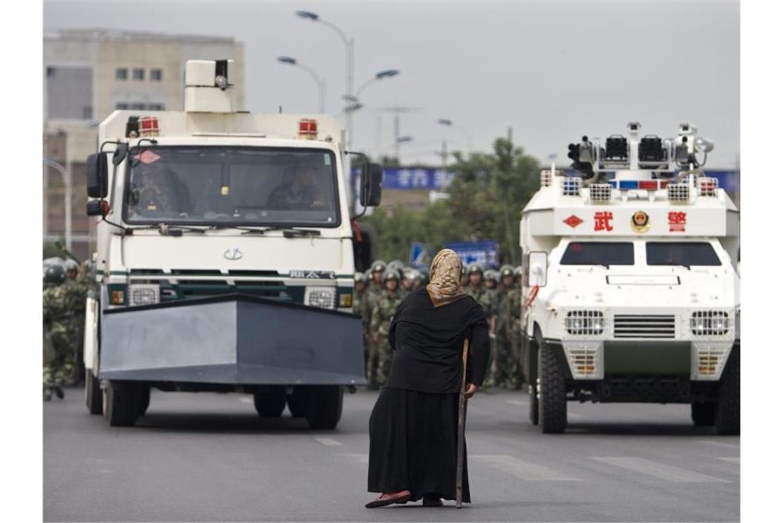 Eine uigurische Frau steht vor gepanzerten Fahrzeugen der Staatsmacht. Foto: Diego Azubel/EPA/dpa