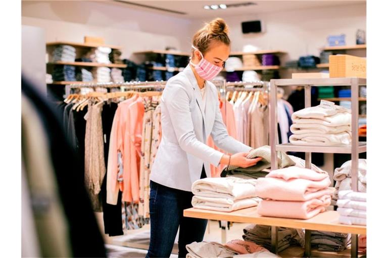 Eine Verkäuferin mit Mund- und Nasenschutz arbeitet in einem Modegeschäft. Der Textilhandel in den deutschen Innenstädten schlägt Alarm. Foto: Rolf Vennenbernd/dpa