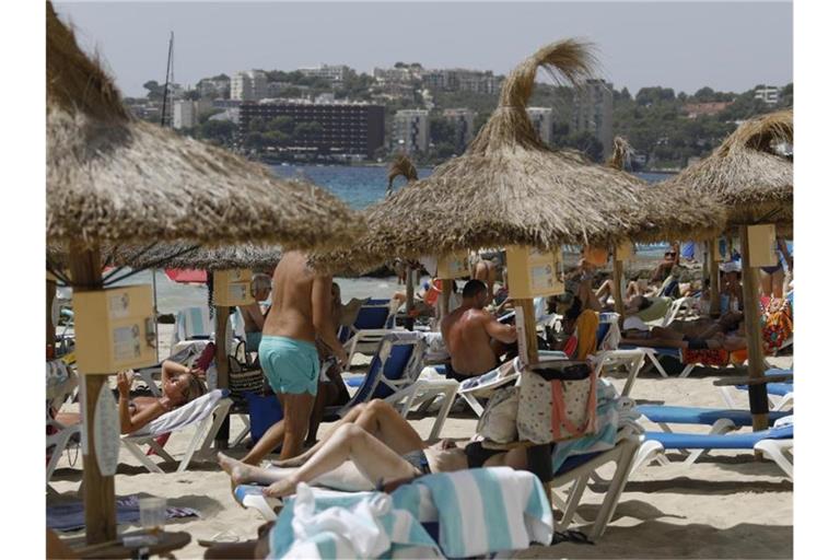 Einheimische und Touristen liegen am Strand Cala Major in Palma de Mallorca. Foto: Clara Margais/dpa