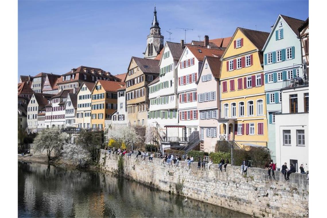 Einige Menschen sitzen auf der Neckarmauer in der Tübinger Innenstadt. Foto: Tom Weller/dpa